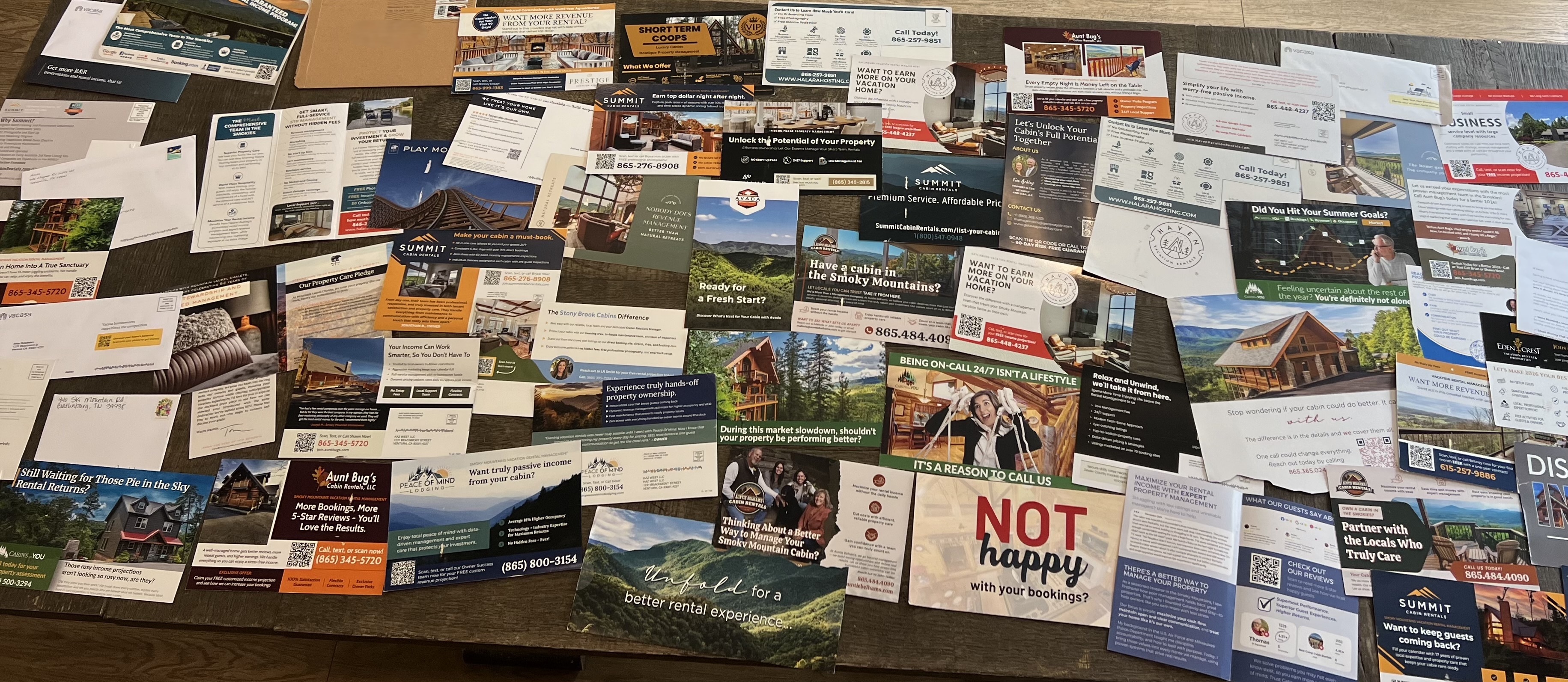 A table covered in dozens of cabin management postcards from competing Smoky Mountain rental companies  - all promising the same things