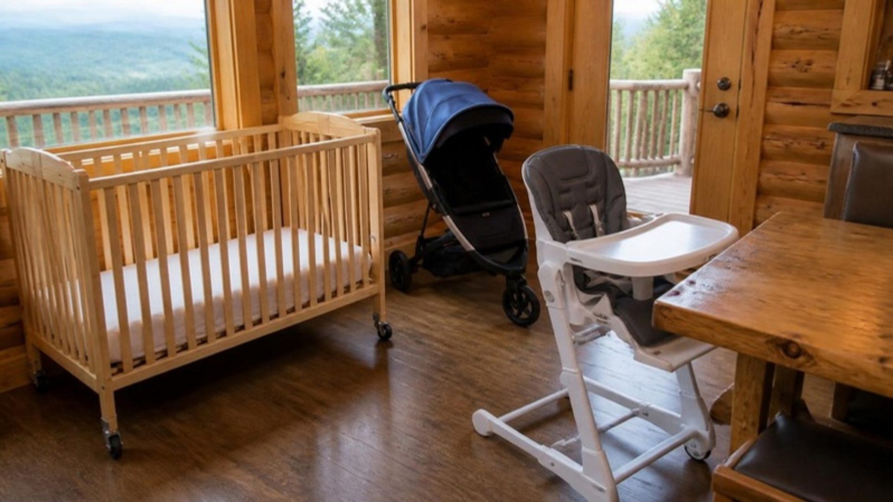 Rented crib, stroller and high chair set up in a knotty-pine cabin with a window view of forested mountains