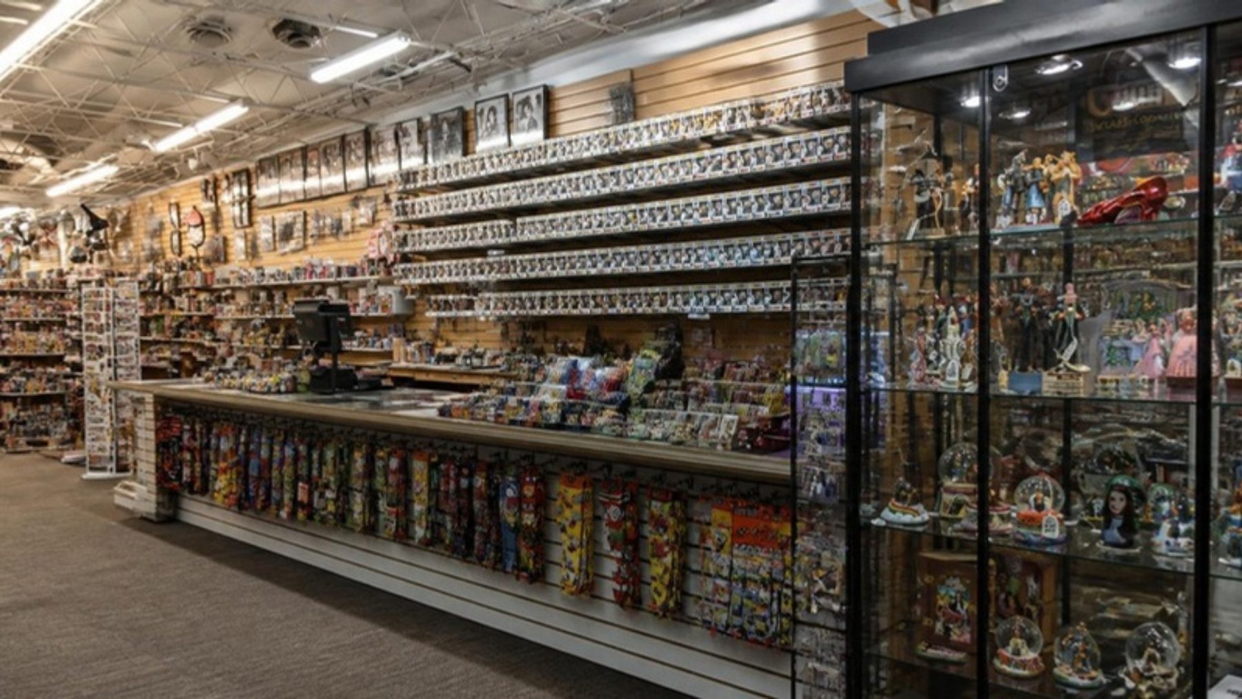 Collectibles shop interior with slatwall shelves stacked with boxed vinyl figures, a long counter and a lighted glass display case of memorabilia