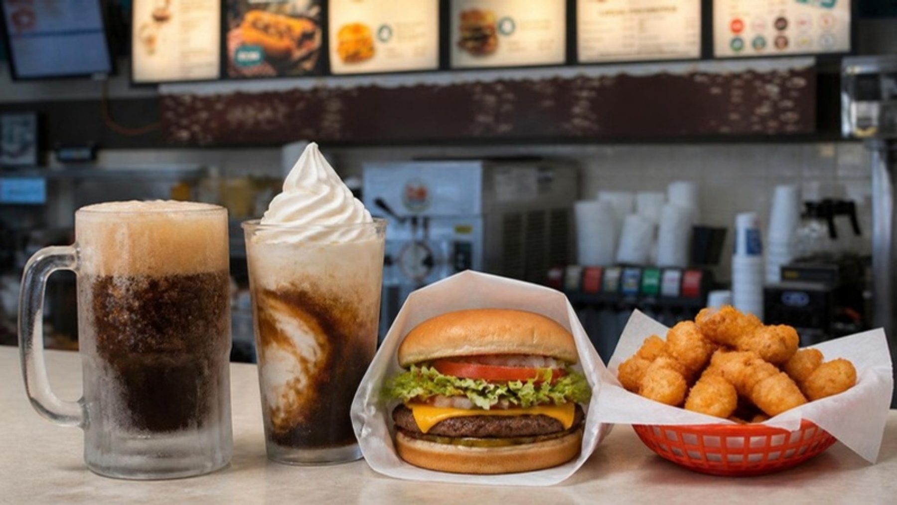 Frosted mug of root beer, a root beer float, a cheeseburger and fried cheese curds on the counter of a casual burger stand