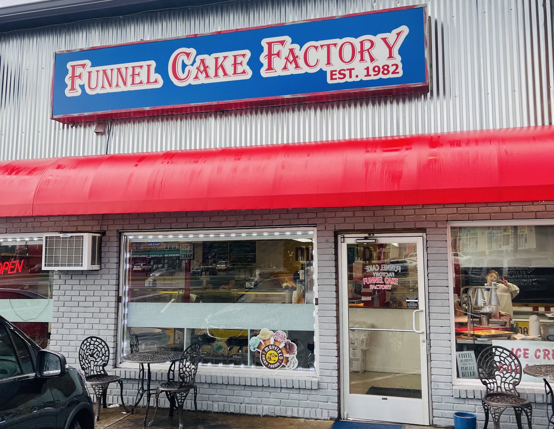 Funnel Cake Factory storefront in Pigeon Forge with its blue "Est. 1982" sign, red awning and bistro chairs out front