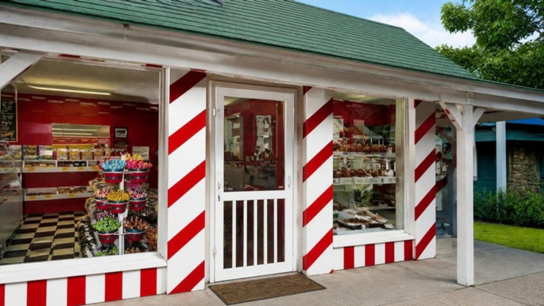Candy shop storefront trimmed in red and white candy-cane stripes with a white screen door and candy displays visible through the windows