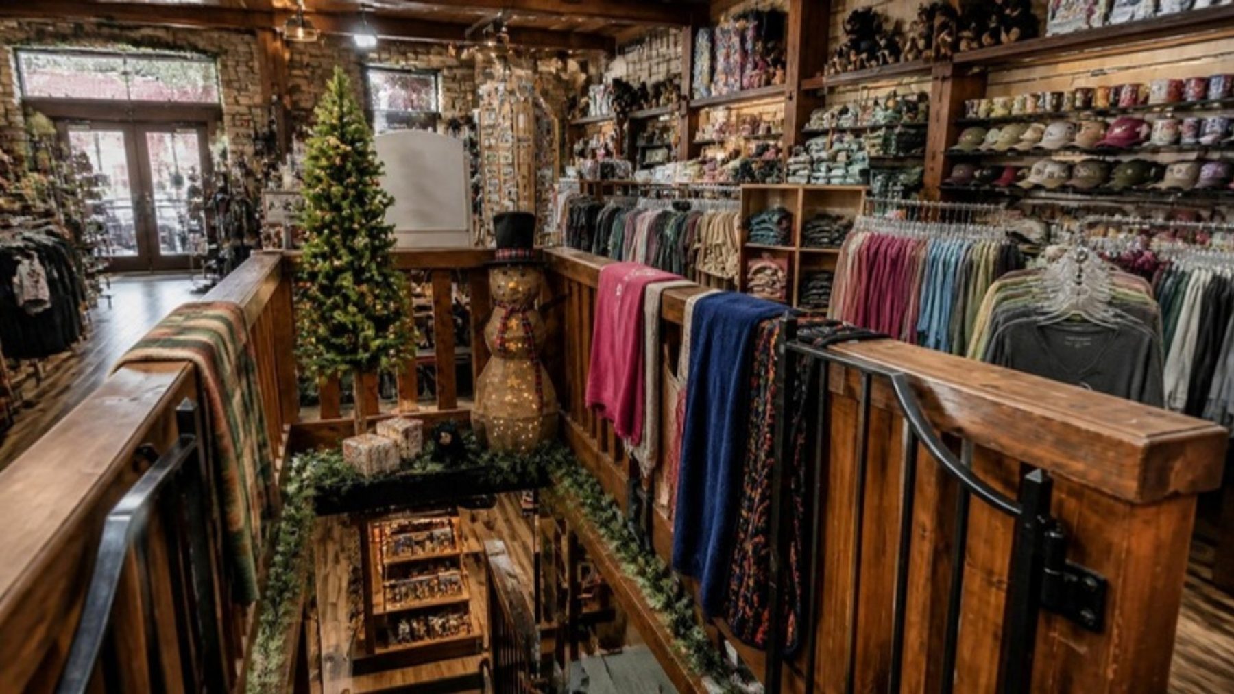 Two-level rustic gift shop interior with wood railings and racks of colorful apparel, hats and souvenirs