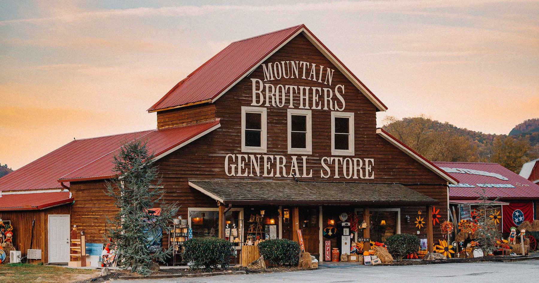 Red-roofed wooden barn storefront of Mountain Brothers General Store decorated for fall at dusk