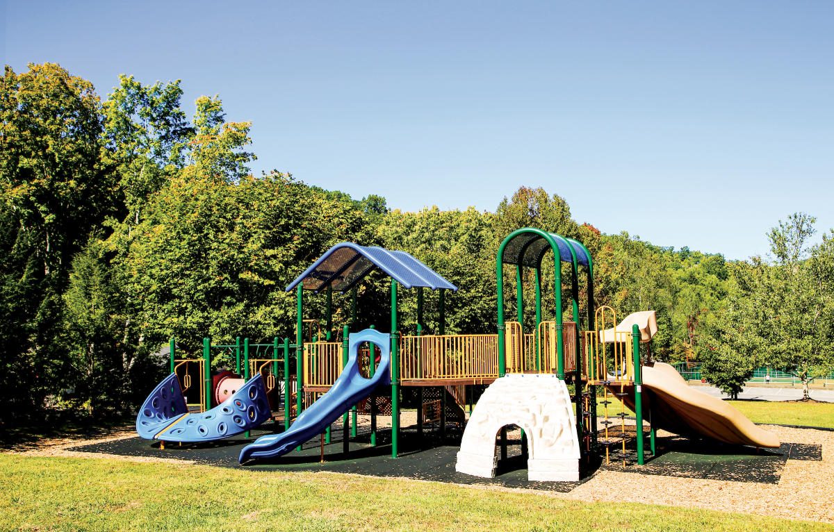 Playground with slides and climbing structures on a lawn ringed by trees at Mynatt Park