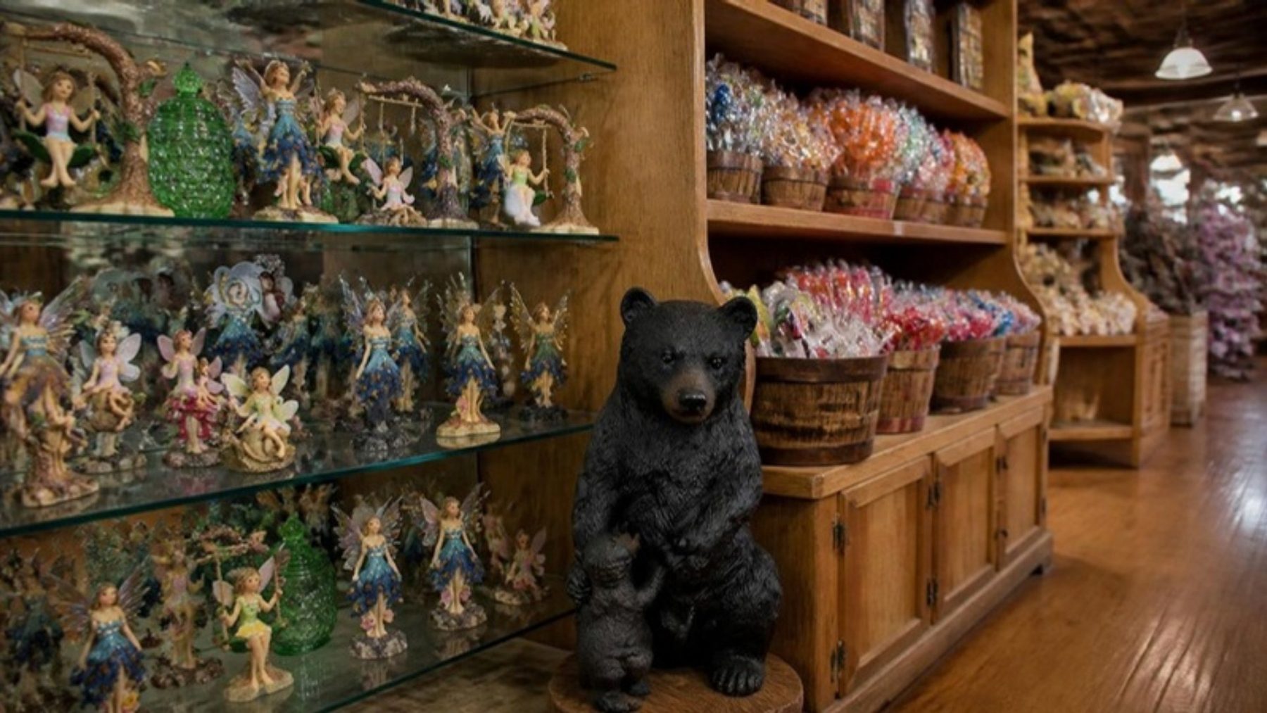 Souvenir shop interior with glass shelves of fairy figurines, a carved black bear statue, and wooden shelves of old-fashioned candy