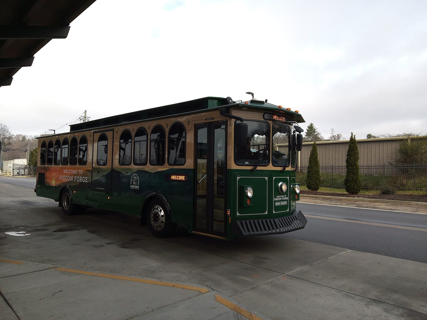 Green and tan Pigeon Forge Mass Transit trolley with a Welcome to Pigeon Forge wrap parked at the trolley station