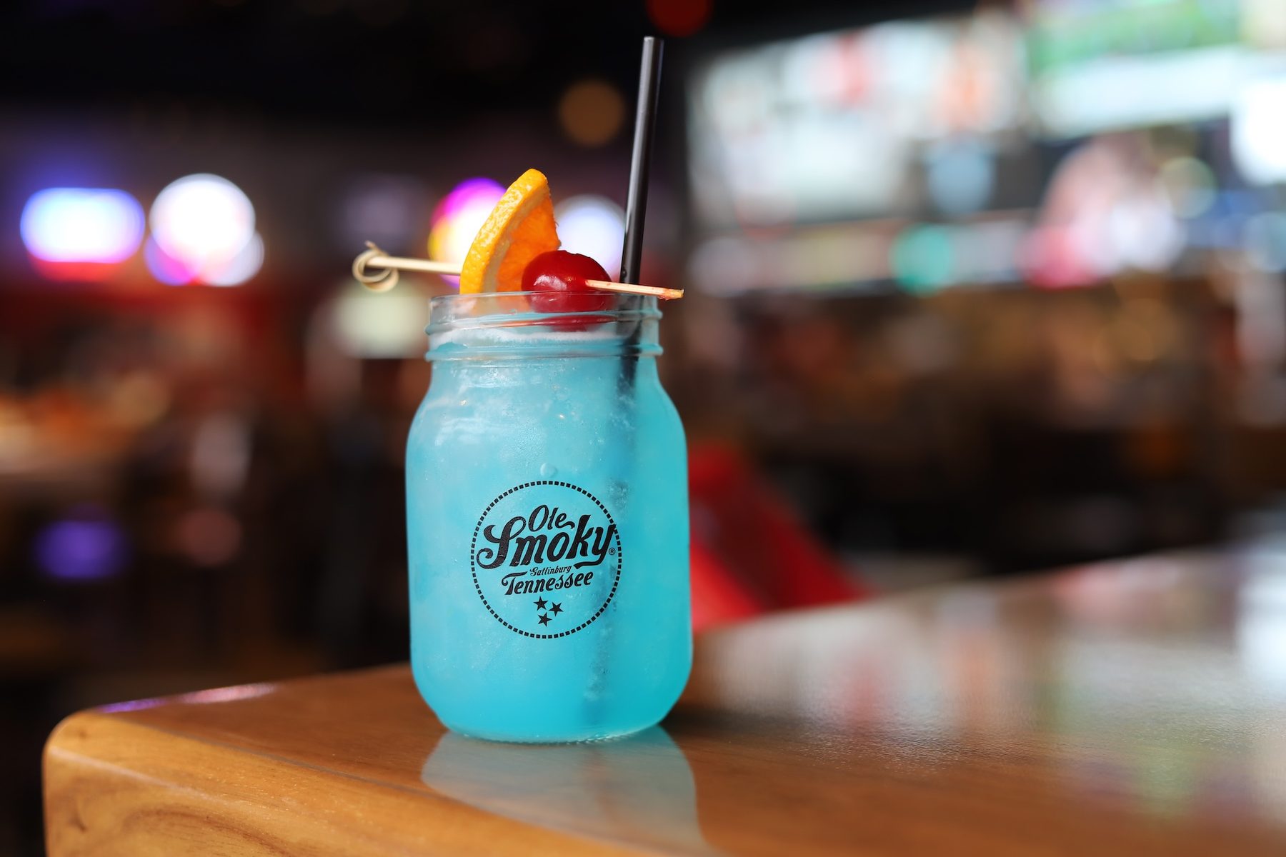 Blue cocktail in a mason jar on the bar at Puckers Sports Grill with TVs glowing behind