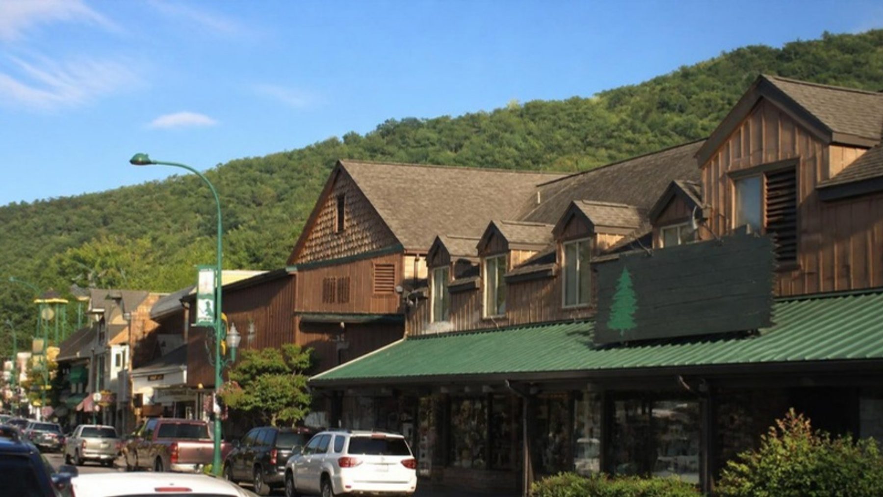 Rustic wood-sided gift shop with a green awning on the Gatlinburg Parkway, with a green mountain ridge rising behind