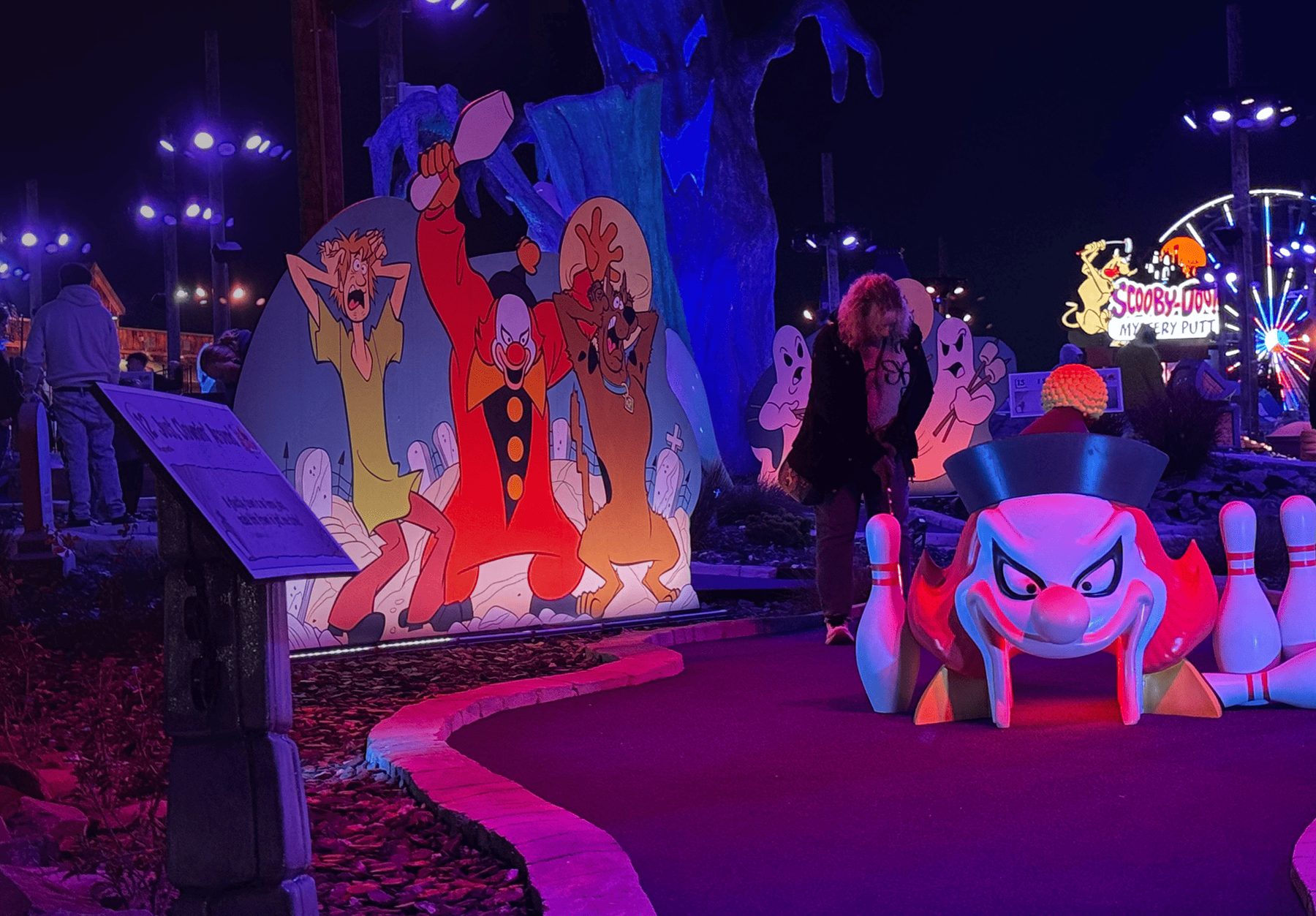 Glow-lit night hole at Scooby-Doo! Mystery Putt with a giant clown bowling-pin obstacle and character cutouts