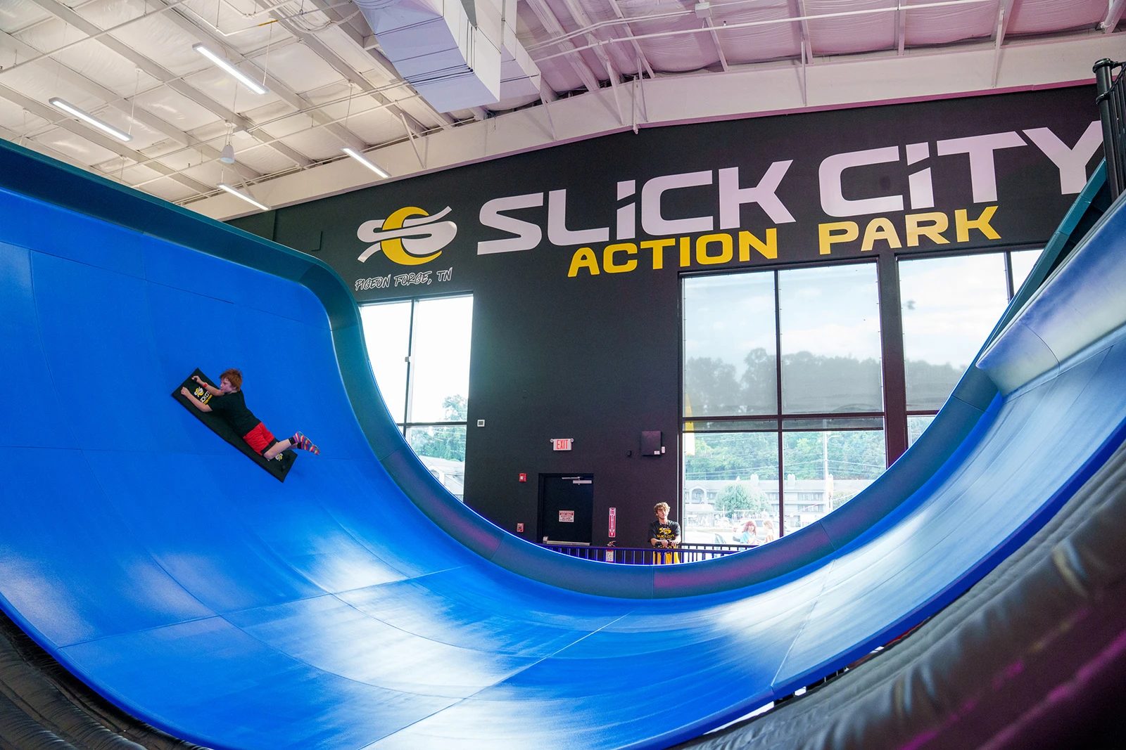 Rider sliding down a giant blue half-pipe slide inside Slick City Action Park