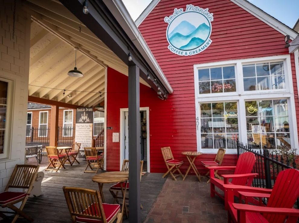 Red clapboard storefront of Smoky Mountain Coffee & Creamery with a covered porch of cafe tables and red Adirondack chairs