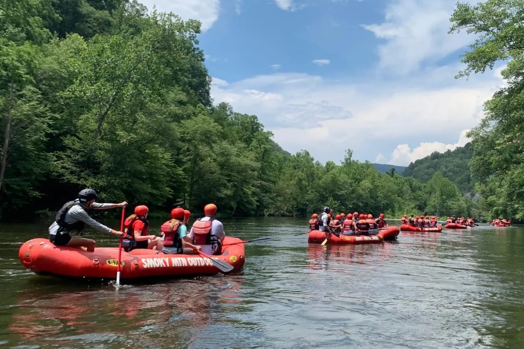 Red Smoky Mountain Outdoors rafts floating a calm stretch of the Pigeon River between forested banks