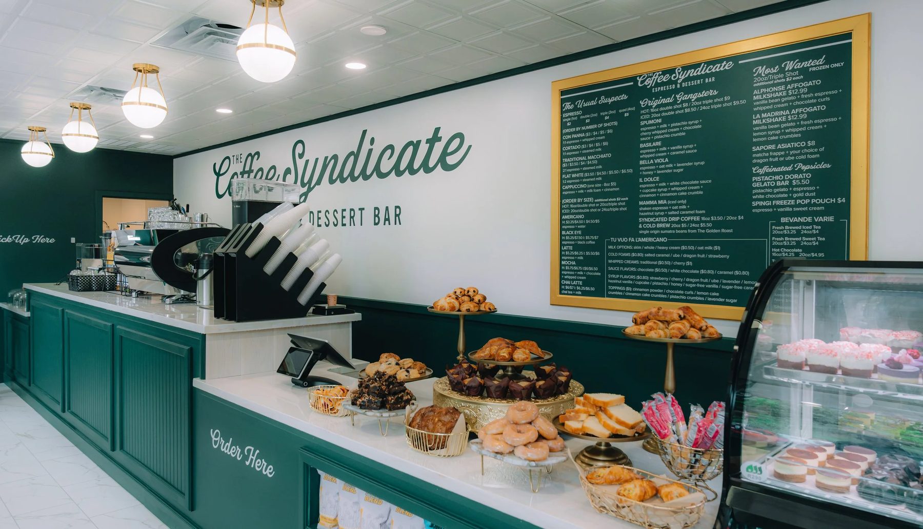 Green-and-white counter and pastry case inside The Coffee Syndicate espresso and dessert bar