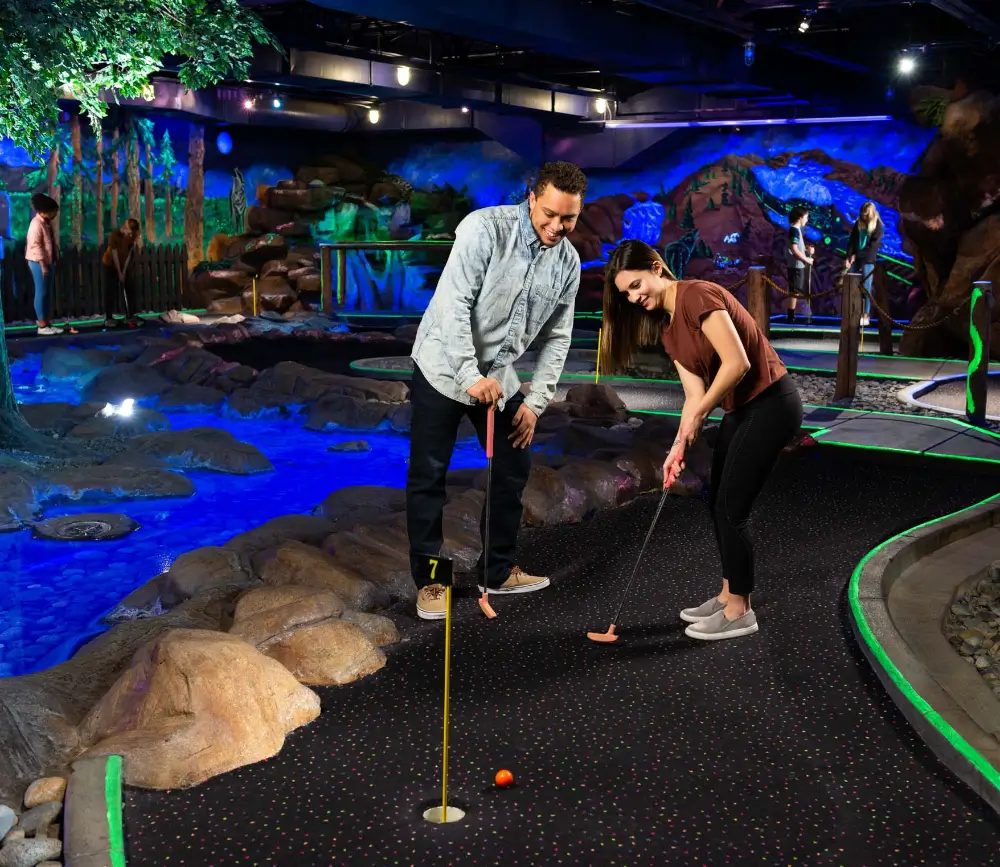Two players putting on the glow-lit indoor mini golf course at The Sweet Spot