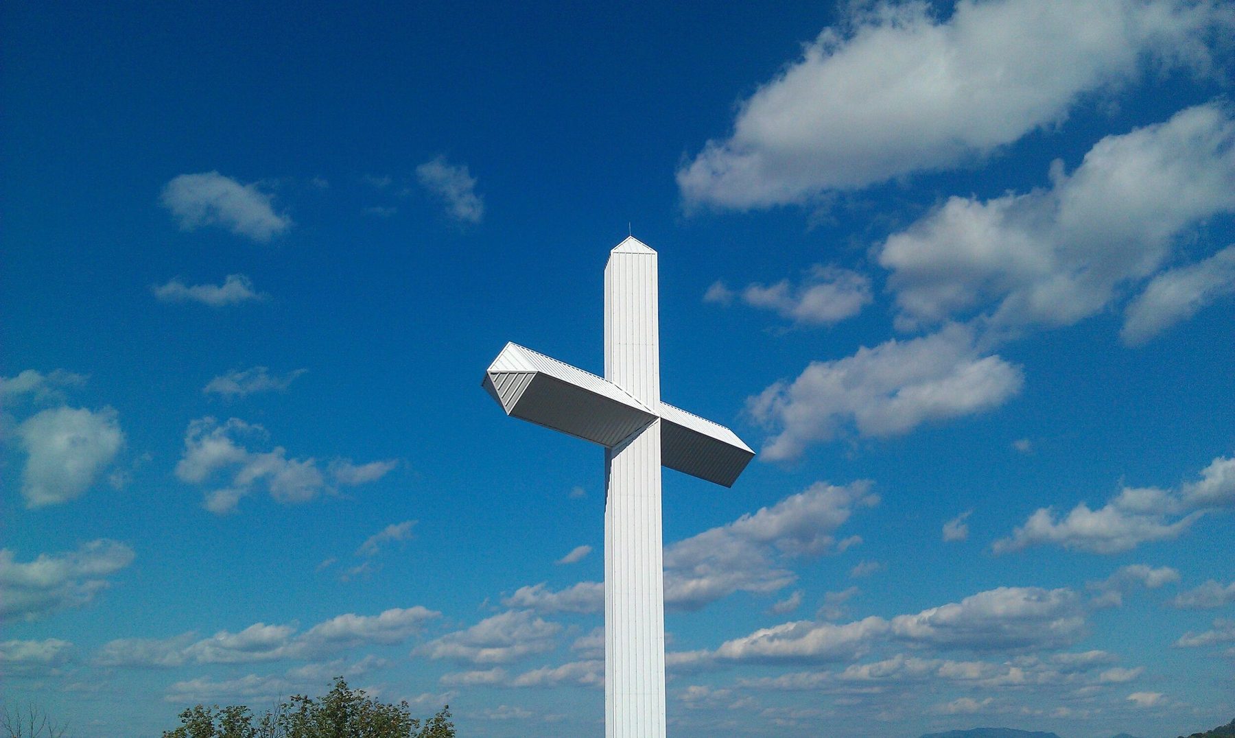 The tall white Cross at Wears Valley against a blue sky with scattered clouds