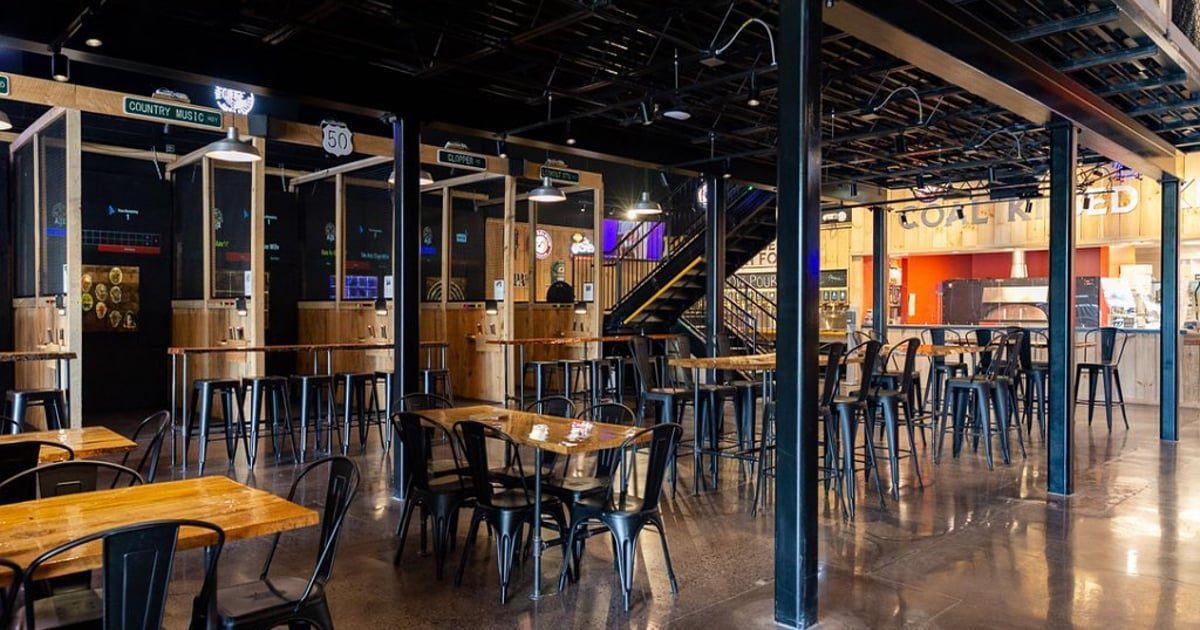 Dining room with wood-top tables, axe-throwing lanes along one wall and the coal-fired pizza counter at the back