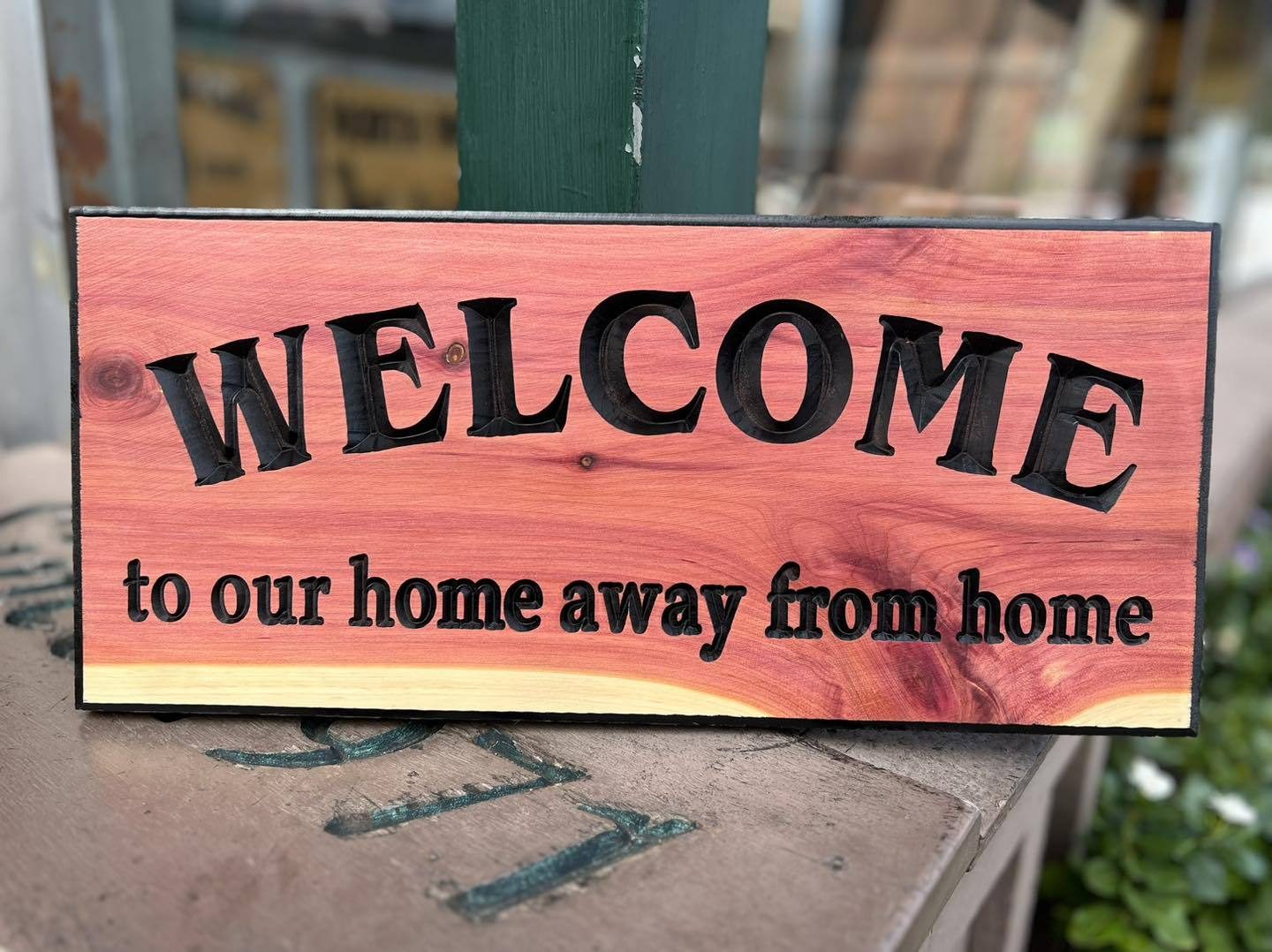 Hand-carved cedar sign reading "Welcome to our home away from home" on a ledge outside the Gatlinburg shop